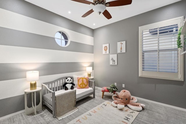 carpeted bedroom featuring a nursery area and ceiling fan