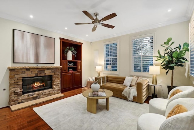 living room with ceiling fan, ornamental molding, a stone fireplace, and light wood-type flooring