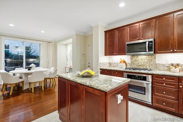 kitchen with tasteful backsplash, a center island, light stone counters, stainless steel appliances, and crown molding