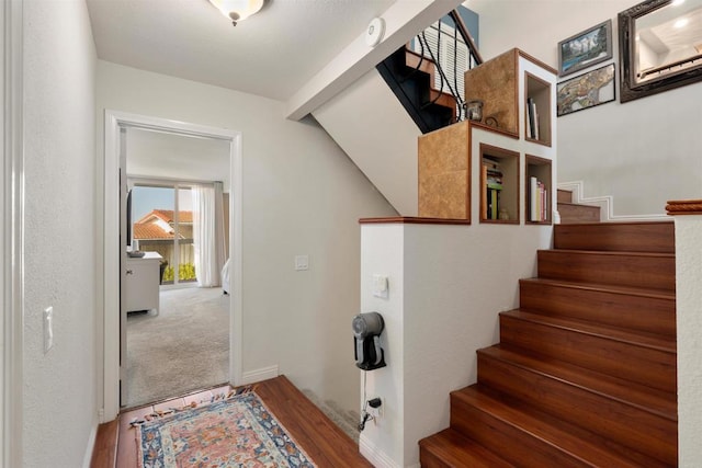 staircase with beam ceiling, baseboards, and wood finished floors