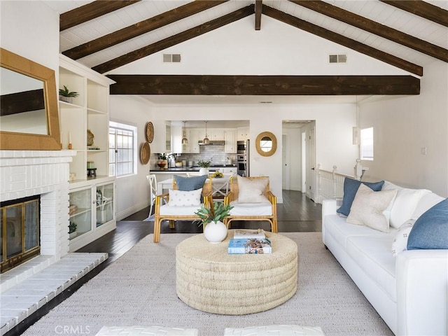 living room with wood-type flooring, sink, a brick fireplace, and vaulted ceiling with beams