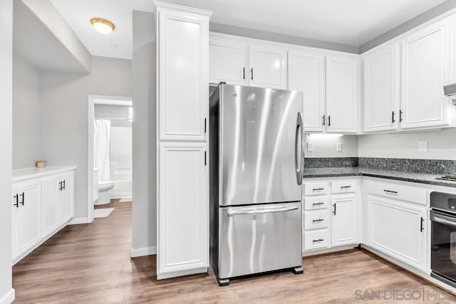 kitchen featuring light hardwood / wood-style flooring, oven, stainless steel refrigerator, and white cabinets