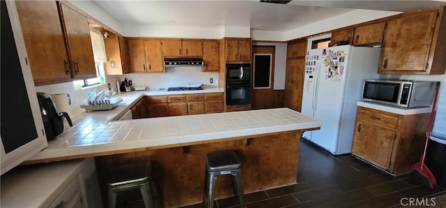 kitchen featuring tile countertops, range hood, black appliances, a kitchen breakfast bar, and kitchen peninsula