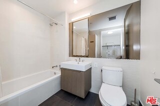 full bathroom featuring vanity, toilet,  shower combination, and tile patterned flooring