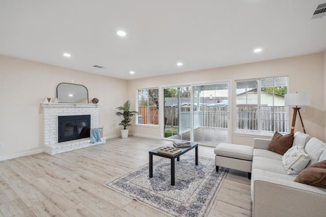 living room featuring a brick fireplace, a healthy amount of sunlight, and light wood-type flooring