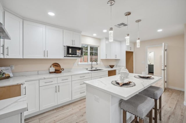 kitchen with built in microwave, white cabinetry, sink, and decorative light fixtures