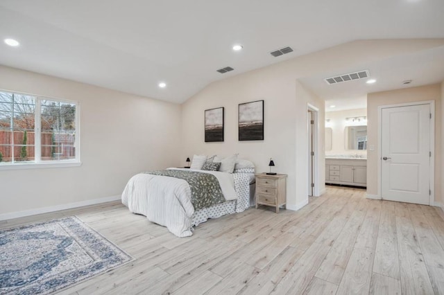 bedroom with ensuite bathroom, lofted ceiling, and light wood-type flooring