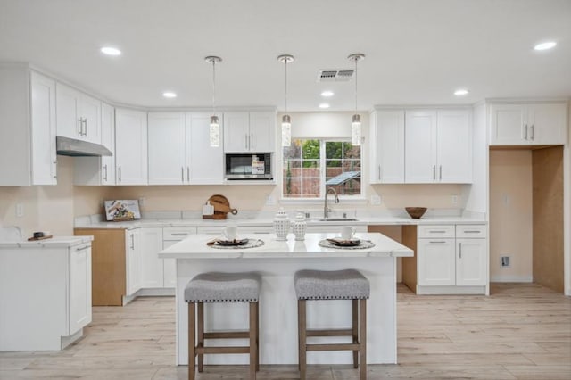 kitchen with stainless steel microwave, hanging light fixtures, white cabinets, and a kitchen island