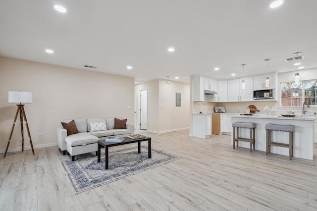 living room with sink, electric panel, and light hardwood / wood-style floors