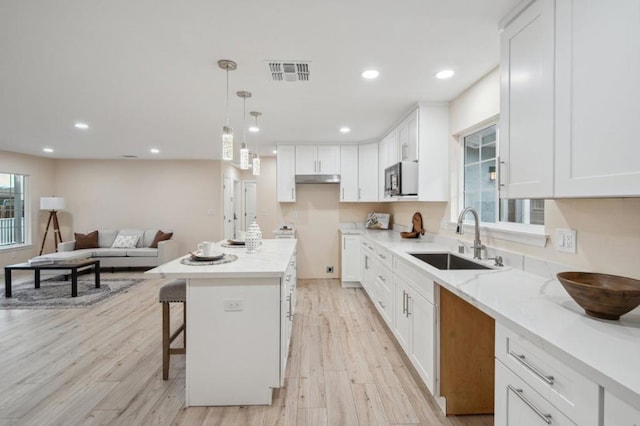 kitchen featuring a kitchen island, white cabinetry, sink, light stone counters, and light hardwood / wood-style floors