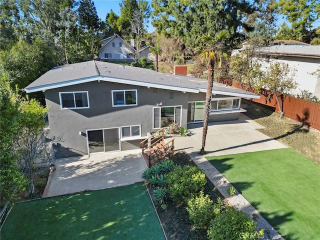 rear view of house with fence, a yard, stucco siding, a chimney, and a patio area