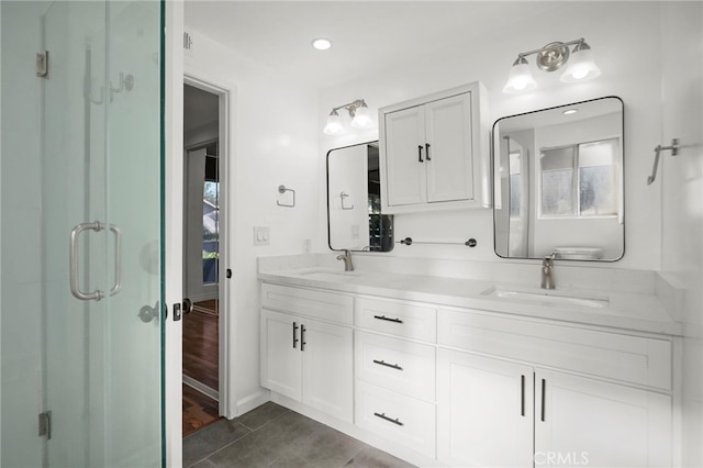 full bath with double vanity, a shower stall, baseboards, and a sink