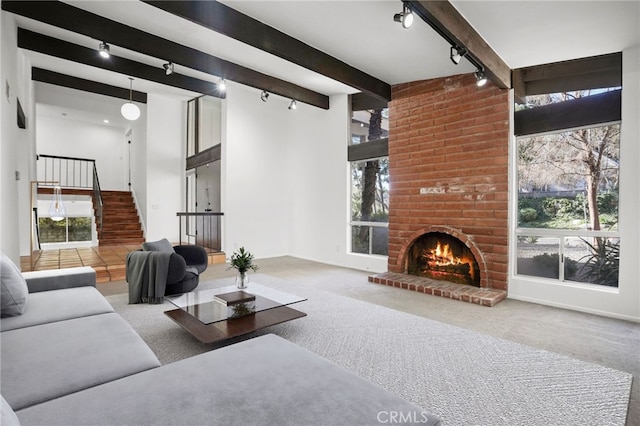 living area featuring a wealth of natural light, carpet, beam ceiling, and a brick fireplace