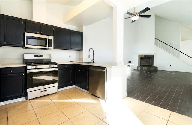 kitchen featuring appliances with stainless steel finishes, high vaulted ceiling, sink, a tiled fireplace, and light tile patterned floors