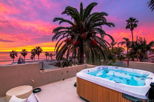 pool at dusk featuring a hot tub and a water view