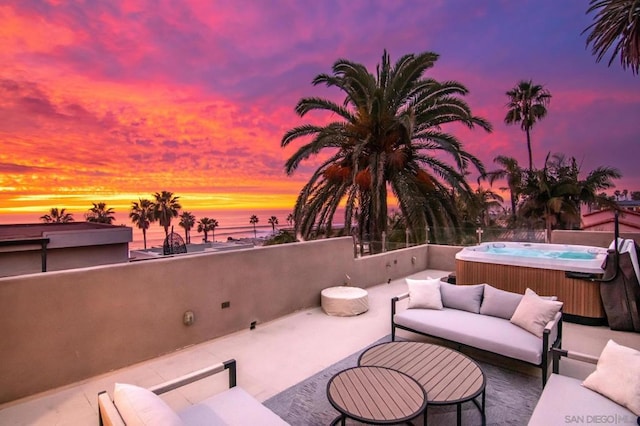 patio terrace at dusk featuring a hot tub, a water view, and an outdoor hangout area