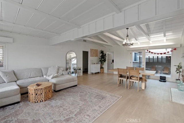 living room featuring vaulted ceiling with beams, a notable chandelier, and light hardwood / wood-style floors