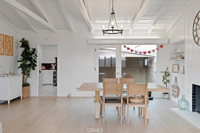 dining room featuring a notable chandelier, light hardwood / wood-style floors, vaulted ceiling with beams, and a brick fireplace