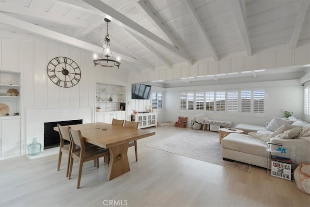 dining space with built in features, vaulted ceiling with beams, light hardwood / wood-style floors, a brick fireplace, and an inviting chandelier