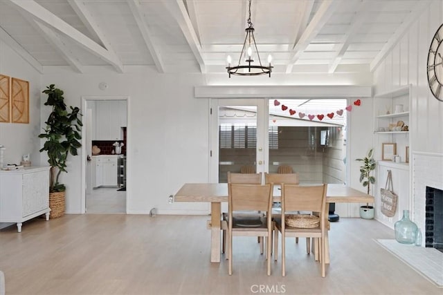 dining space featuring vaulted ceiling with beams, an inviting chandelier, a fireplace, and wood finished floors