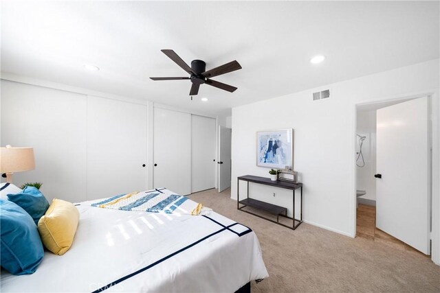 bedroom with ceiling fan, light carpet, and two closets