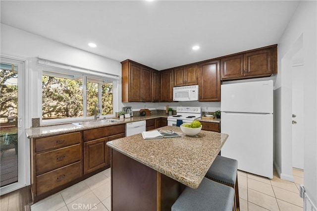 kitchen with sink, a center island, light stone countertops, dark brown cabinets, and white appliances