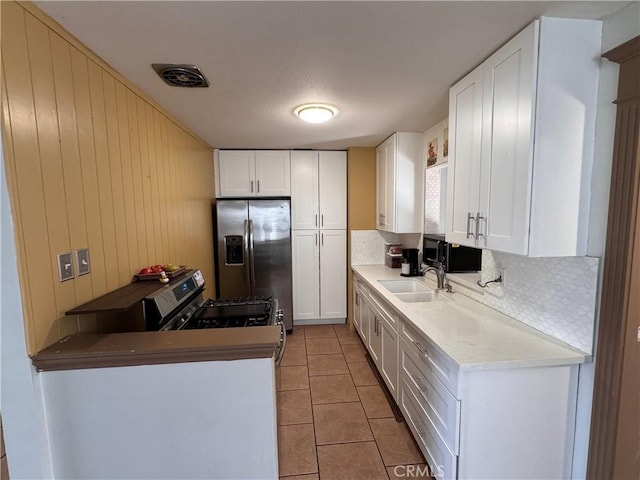 kitchen featuring sink, light tile patterned floors, appliances with stainless steel finishes, white cabinets, and wood walls