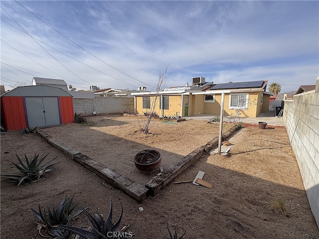 back of house featuring solar panels, a patio, a fire pit, central AC unit, and a storage shed