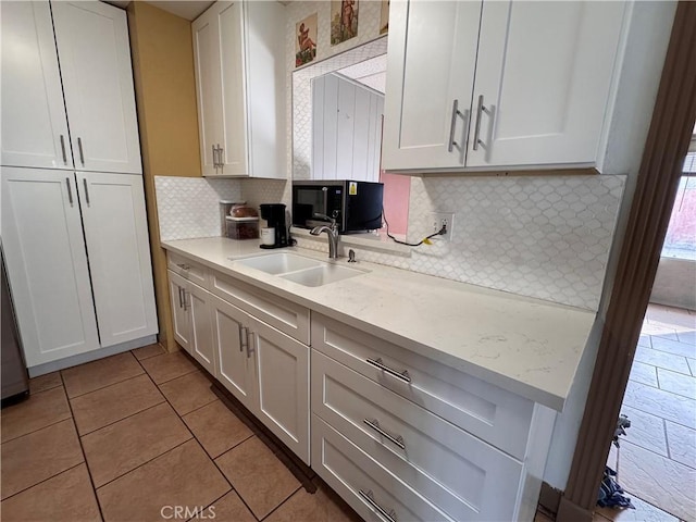 1704 Sunrise Rd, Barstow, CA 92311 - kitchen with black microwave, a sink, white cabinetry, backsplash, and light tile patterned floors
