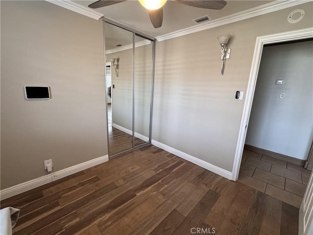 unfurnished bedroom with crown molding, ceiling fan, dark wood-type flooring, and a closet