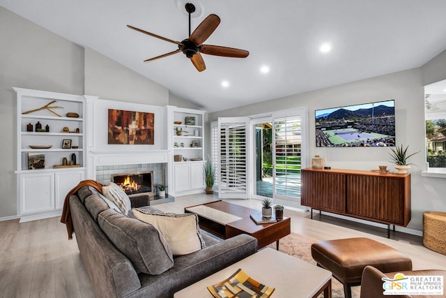 living room featuring vaulted ceiling, light hardwood / wood-style flooring, built in features, a tile fireplace, and ceiling fan