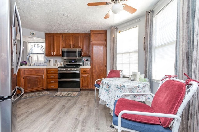 kitchen with sink, a textured ceiling, ceiling fan, stainless steel appliances, and light hardwood / wood-style floors