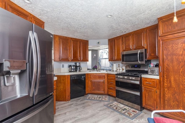 kitchen with sink, hanging light fixtures, light hardwood / wood-style floors, stainless steel appliances, and a textured ceiling