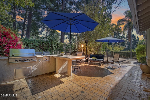 patio terrace at dusk featuring an outdoor living space, an outdoor kitchen, and a grill