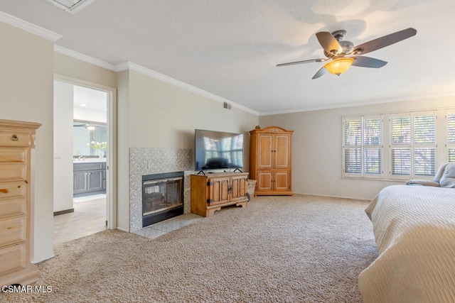 carpeted bedroom featuring a tiled fireplace, ceiling fan, crown molding, and ensuite bath