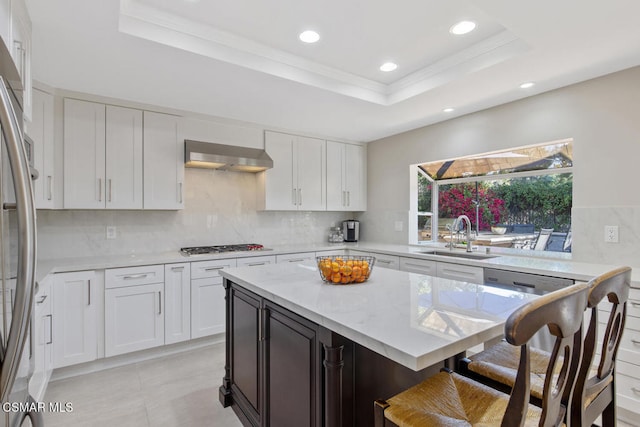 kitchen with wall chimney exhaust hood, sink, white cabinetry, a raised ceiling, and decorative backsplash