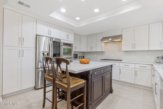 kitchen with appliances with stainless steel finishes, a kitchen breakfast bar, a raised ceiling, a kitchen island, and white cabinets