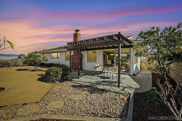 back house at dusk with a pergola and a patio