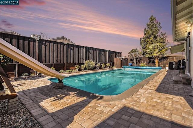 pool at dusk featuring a patio and a water slide