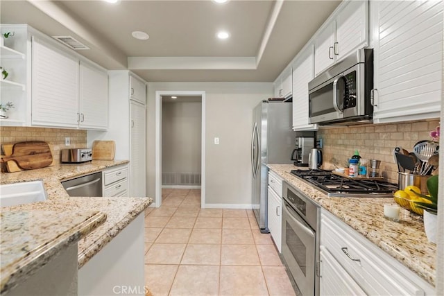 kitchen with light stone counters, white cabinetry, light tile patterned floors, stainless steel appliances, and decorative backsplash