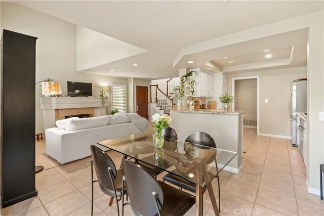 dining area featuring a tray ceiling, sink, a tile fireplace, and light tile patterned floors