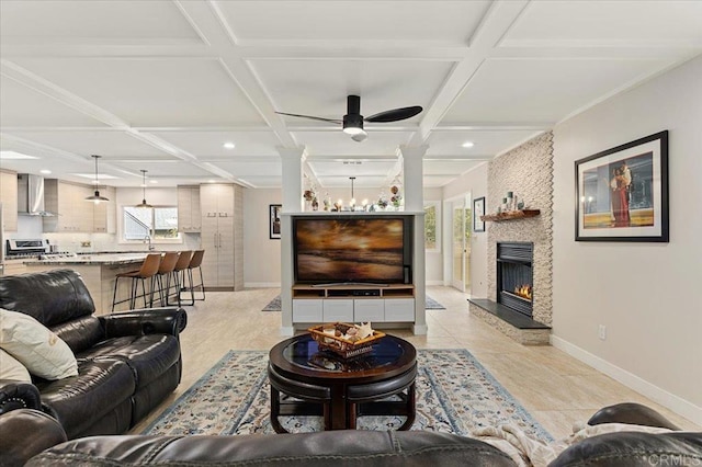 living area with baseboards, a stone fireplace, coffered ceiling, a ceiling fan, and ornate columns