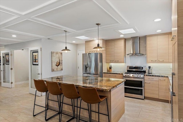 kitchen with light brown cabinetry, a center island, appliances with stainless steel finishes, a breakfast bar area, and wall chimney exhaust hood