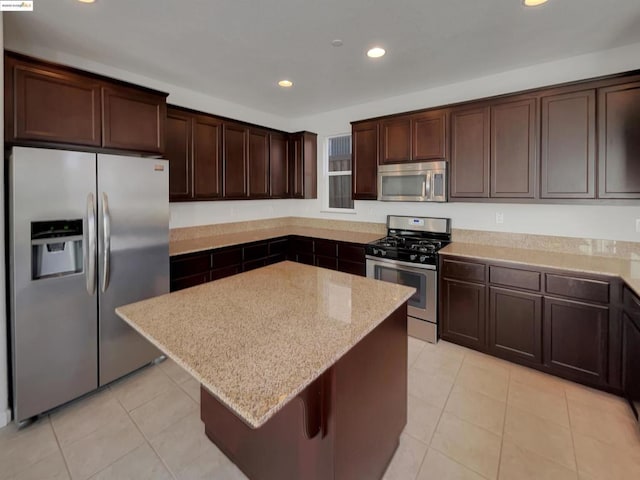 kitchen with appliances with stainless steel finishes, a center island, light tile patterned floors, dark brown cabinetry, and light stone countertops