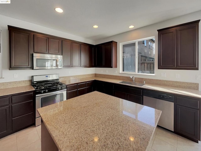 kitchen with sink, appliances with stainless steel finishes, light stone counters, a kitchen island, and light tile patterned flooring