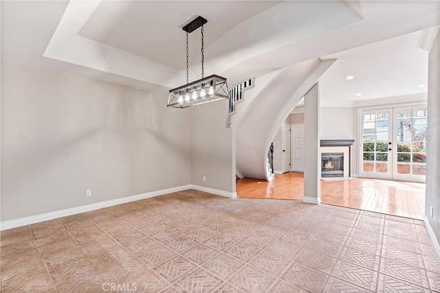 unfurnished dining area featuring a glass covered fireplace, a tray ceiling, baseboards, and recessed lighting