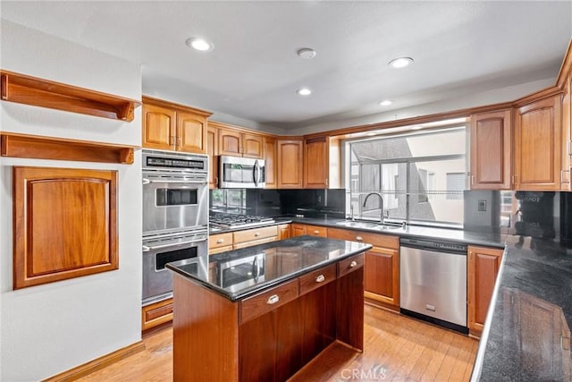 kitchen featuring light wood finished floors, dark stone countertops, appliances with stainless steel finishes, and a sink