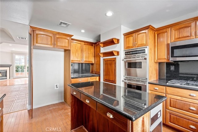 kitchen with visible vents, appliances with stainless steel finishes, a kitchen island, dark stone countertops, and light wood-type flooring