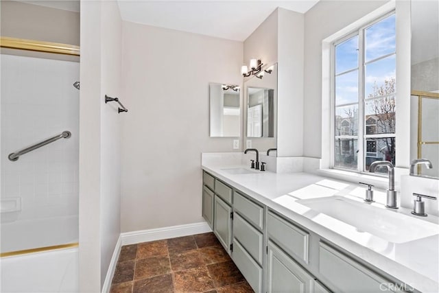 full bath with stone finish floor, a sink, baseboards, and double vanity