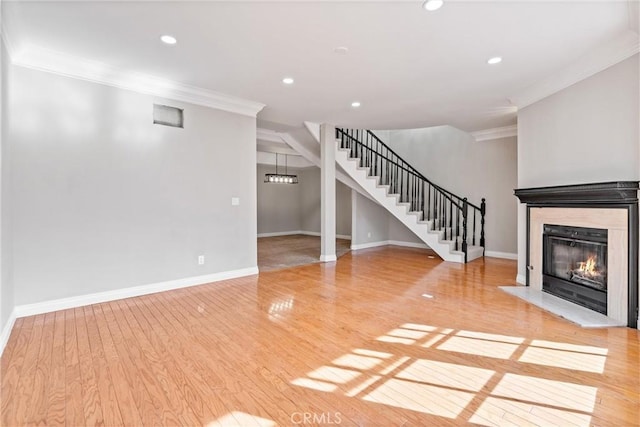 unfurnished living room featuring a glass covered fireplace, crown molding, stairway, and light wood finished floors